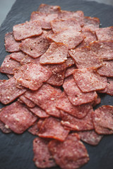 Thinly sliced sausage slices on a black stone board. 