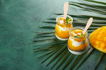 Jars with tasty mango dessert on color background