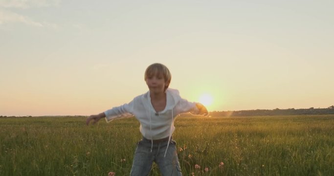 Happy child with raised hands jumps while sunset  in the summer. Happy  7 year old cheerful boy goes and jumps  on field while sunset. Happiness concept.  Active  boy on the nature. Slow motion.