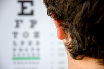 Concept photo of myopia or nearsightedness as diseases of eye and the optical system. In the background blurry fuzzy table for testing visual acuity, in the front - head of the person in focus closeup - obrazy, fototapety, plakaty