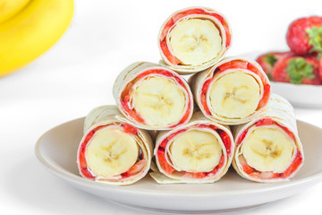 Vegetarian strawberry banana rolled pancakes in shape of pyramidon white background