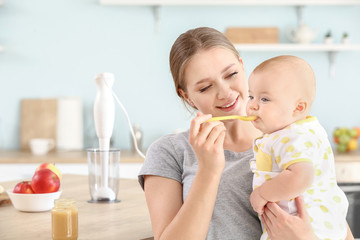 Mother feeding her little baby in kitchen at home