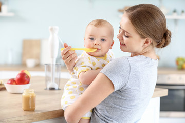 Mother feeding her little baby in kitchen at home