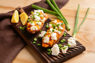 Baked sweet potato with cheese and arugula on wooden board
