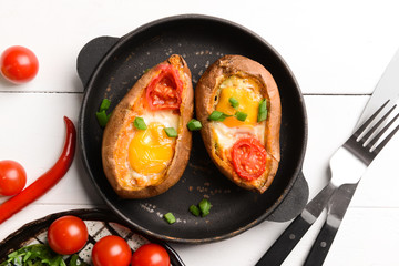 Baked sweet potato with egg and tomato on white table