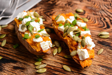 Baked sweet potato with cheese and arugula on wooden board