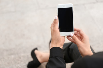Young businesswoman with mobile phone sitting on stairs outdoors