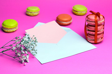 Pink macaroons with white open envelope and white wild flowers on pink background. Roman  tic letter concept.