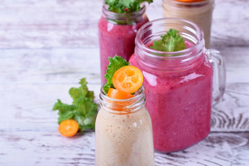 Berry and fruit smoothies in glass jars topped with mint and kumquat slices against the white wooden background