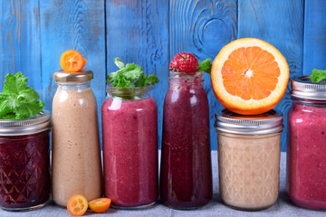 Assortment of different smoothies topped with fruits, berries and mint on the table against the blue background