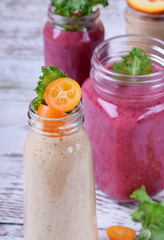 Berry and fruit smoothies in glass jars topped with mint and kumquat slices against the white wooden background