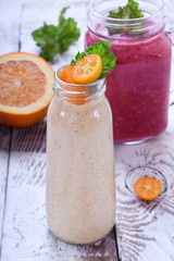 Berry and fruit smoothies in glass jars topped with mint and kumquat slices against the white wooden background