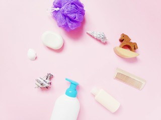 . Flat lay beauty photo. Shampoo, soap, purple puff sponge and toy wooden horse on a pink background
