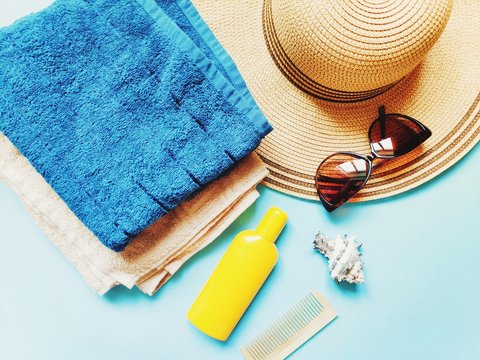 Beach essentials and accessories for women. Blue and beige terry towels, wicker hat, sunglasses and sunscreen lotion. Summer holidays flat lay composition photo