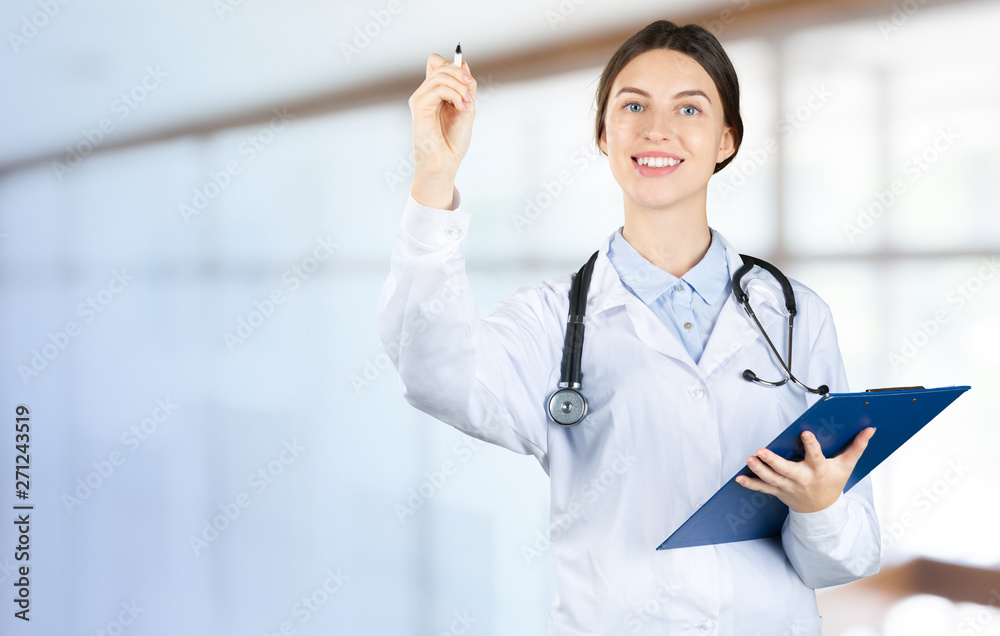 Canvas Prints Smiling female doctor in white coat with stethoscope and clipboard pointing finger