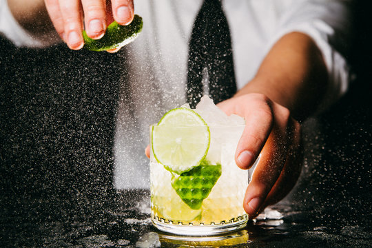 Close-up of professional bartender squeezing lime making Caipirinha cocktail