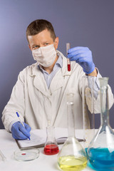 A male scientist in white uniform and mask writes down his research notes after viewing blood tests in a laboratory. The concept of health and biotechnology