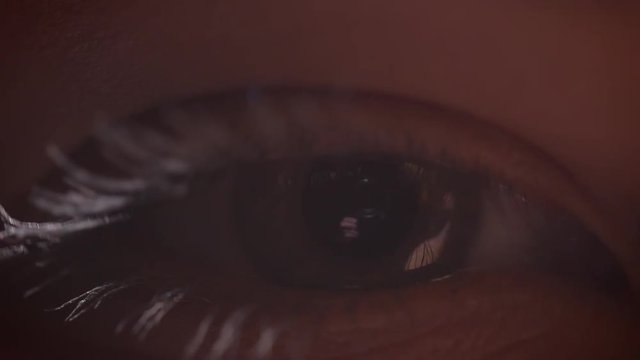 Close-up shoot of eye blinking with the reflection of photographer with camera in it in glowing lighting.