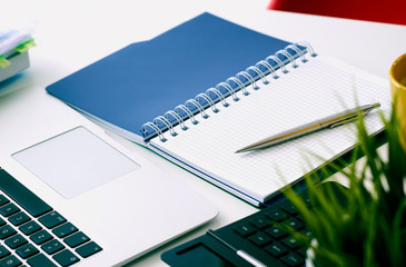 Closeup of white desktop with laptop, coffee cup, notepads, pen, calculator and other items.