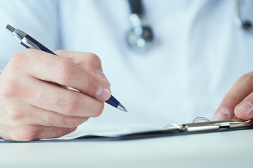 Male physician medicine doctor or pharmacist writing prescription on special form sitting at worktable. Medical care, pharmacy or health insurance concept.