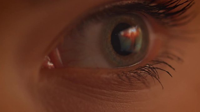 Close-up shoot of eye watching rightwards being concentrated in red and yellow light.