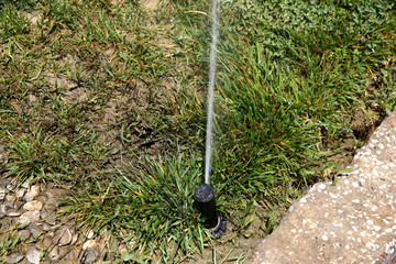 Automatic watering - sprinkler system. Sprinkler head spraying water on green lawn with bokeh backgound. Irrigation system - technique of watering in garden. Lawn sprinkler spraying water over green 