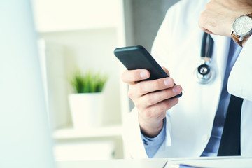 Male doctor in white coat is using a modern smartphone device with touch screen. Doctor hands with mobile phone.