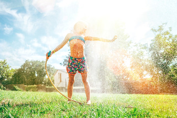 Cute little girl refresh herself from garden watering hose