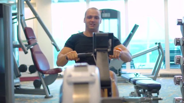 Young athlete makes an exercise on rowing simulator in gym
