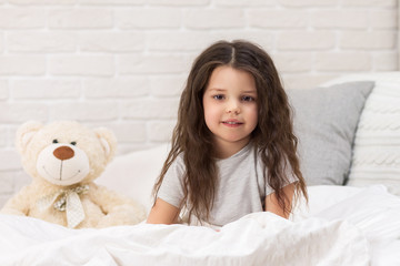 adorable happy little child girl with teddy bear in bed in morning.