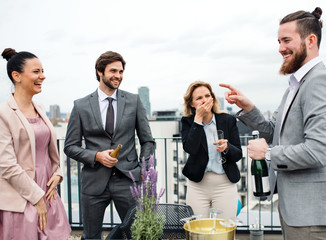 A group of joyful businesspeople having a party outdoors on roof terrace in city.