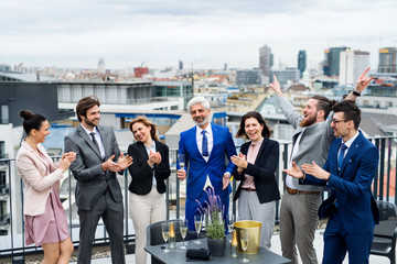 A group of joyful businesspeople having a party outdoors on roof terrace in city.