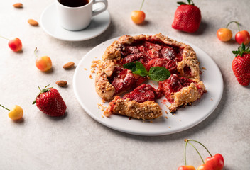 homemade strawberry galleta (biscuit) on a white plate on a light marble backdrop, strawberries and cherries as part of composition