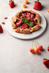 homemade strawberry galleta (biscuit) on a white plate on a light marble backdrop, strawberries and cherries as part of composition