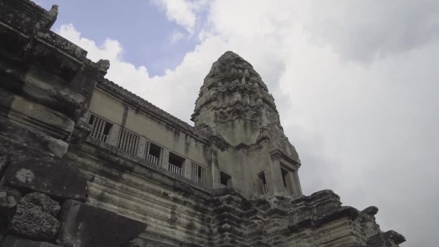 Looking up at a tower of the central shrine at Angkor Wat against a blue sky with puffy clouds.