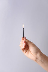 Female hand with burning match on light background