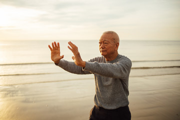 Asian Senior old man practice Tai chi and Yoga pose on the beach sunrise