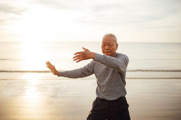 Fototapeta na wymiar Asian Senior old man practice Tai chi and Yoga pose on the beach sunrise