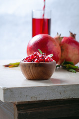 Pomegranate seeds on live wooden bowl with juice fruits and leaves on marble table.