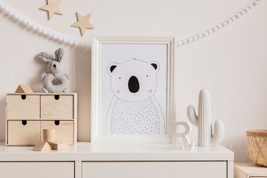 Stylish and cozy childroom with white mock up photo frame, wooden accessories, toys,  plush rabbit, cacti, rattan basket and white garland and stars on the white wall. Bright and sunny interior. 