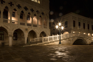 Bridge via the Palace channel, a lamp and a wall of Doges Palace at night during a rain, Venice