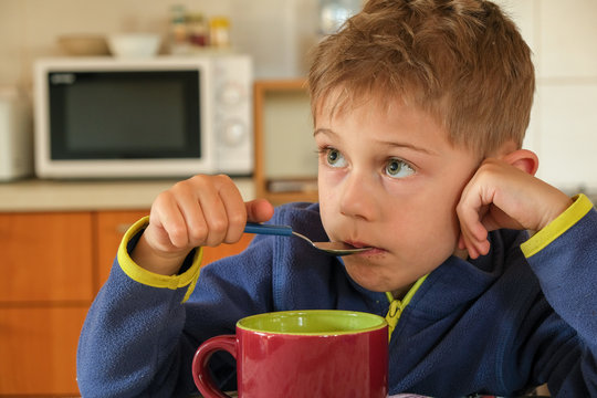 child has breakfast with a red cup and a spoon in his mouth