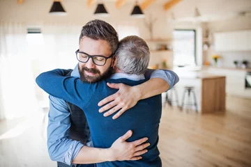 Foto op Plexiglas An adult son and senior father indoors at home, hugging. © Halfpoint