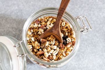 Homemade granola with pecan nuts in glass jar, selective focus, gray background