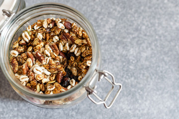 Homemade granola with pecan nuts in glass jar, selective focus, gray background