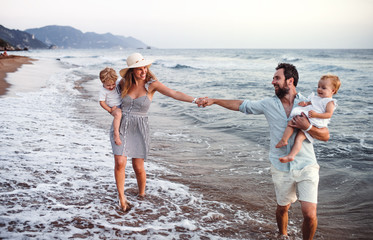 Young family with two toddler children walking on beach on summer holiday.