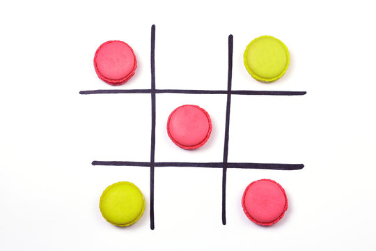 Tic-tac-toe. Different color macaroons and hand drawn black cells on white background. Logical game concept.