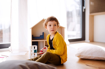 A small girl playing with wooden house on the floor at home.