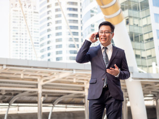 Businessman 50-55 year old talking and smile with smartphone at outdoor in the city. Businessmen use smartphones and technology for communication and work.