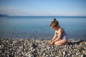 Fototapeta na wymiar Girl on the sea with pebbles, one child on beach